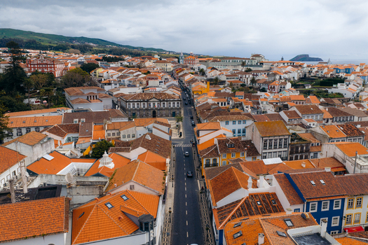 Aerial view of the historic center with orange tiled rooftops colorful facades and a central road under a cloudy sky in Angra do Heroismo Azores Portugal.