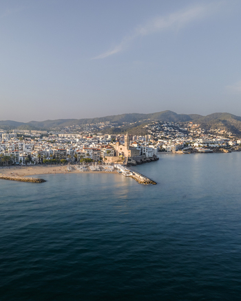 Aerial view of the Church of Sant Bartomeu i Santa Tecla overlooking the Mediterranean Sea sandy beaches and white coastal buildings in Sitges Catalonia Spain. Aerial view of the Church of Sant Bartomeu i Santa Tecla overlooking the Mediterranean Sea sandy beaches and white coastal buildings in Sitges Catalonia Spain.