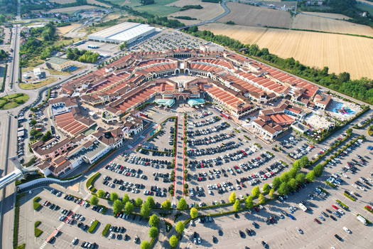 Aerial view of the Designer Outlet Serravalle featuring its circular architectural layout red tiled roofs and large parking lots in Serravalle Scrivia Piemonte Italy. Aerial view of the Designer Outlet Serravalle featuring its circular architectural layout red tiled roofs and large parking lots in Serravalle Scrivia Piemonte Italy.