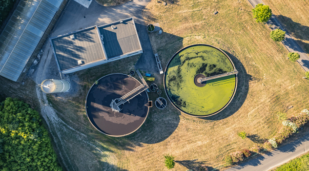 Aerial view of circular clarifier tanks at a wastewater treatment plant with industrial buildings and surrounding green landscape in Le Pouzin Auvergne Rhone Alpes France.