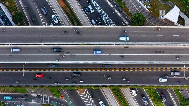 Aerial view of a multi lane highway overpass with cars and motorcycles moving along the road surrounded by urban infrastructure and greenery in Jakarta Indonesia.