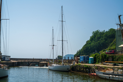 View of a white sailing boat moored in the historic Charlestown Harbour with stone quays lush green hills and clear blue sky in Charlestown Cornwall United Kingdom. View of a white sailing boat moored in the historic Charlestown Harbour with stone quays lush green hills and clear blue sky in Charlestown Cornwall United Kingdom.