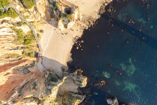 Aerial view of the dramatic limestone cliffs golden sandy beach and turquoise waters of the coastline in Lagos Faro District Portugal.