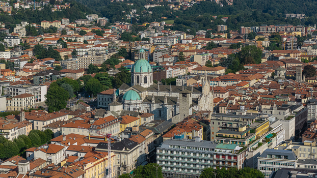 Aerial view of the historic Como Cathedral with its distinctive green dome surrounded by dense urban rooftops and buildings in Como Lombardy Italy.