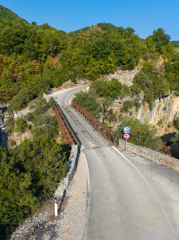 Aerial view of the metal truss bridge spanning the Osumi Canyon surrounded by lush green trees and rocky cliffs along a winding road in Dhores Berat County Albania.