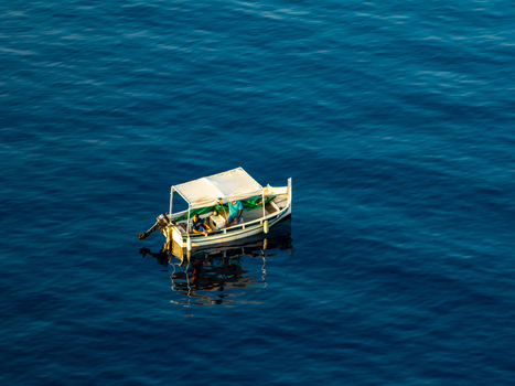 Aerial view of a small white boat adrift on the deep blue sea its reflection shimmering in the sunlight Ghajnsielem gozo Malta. Aerial view of a small white boat adrift on the deep blue sea its reflection shimmering in the sunlight Ghajnsielem gozo Malta.