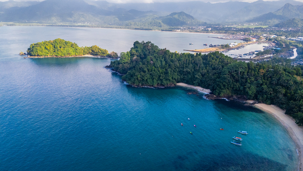 Aerial view of Prigi Beach with lush green hills clear blue water and small fishing boats along the coastline in Kecamatan Watulimo Jawa Timur Indonesia. Aerial view of Prigi Beach with lush green hills clear blue water and small fishing boats along the coastline in Kecamatan Watulimo Jawa Timur Indonesia.