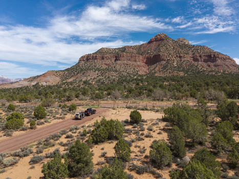 Aerial view of an SUV pulling a teardrop camper trailer on a dirt road on Gooseberry Mesa with the red rock cliffs of Zion National Park in the background Hurricane Utah United States. Aerial view of an SUV pulling a teardrop camper trailer on a dirt road on Gooseberry Mesa with the red rock cliffs of Zion National Park in the background Hurricane Utah United States.