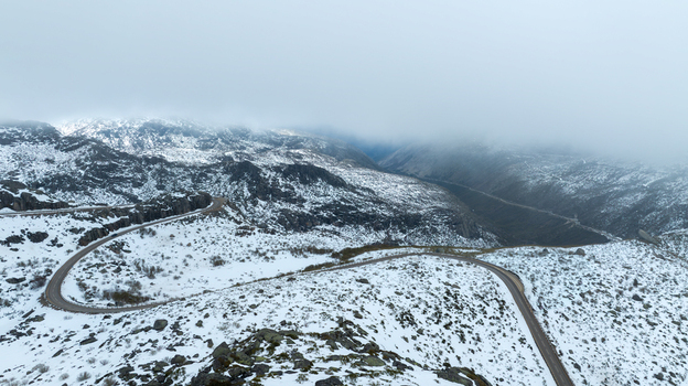 Aerial view of the winding mountain road near the glacial valley deck with snow covered slopes under a misty sky Loriga Guarda District Portugal. Aerial view of the winding mountain road near the glacial valley deck with snow covered slopes under a misty sky Loriga Guarda District Portugal.