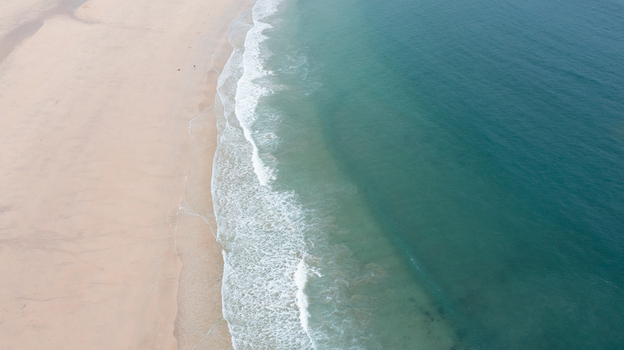 Aerial view of Harlyn Bay Beach with gentle white waves breaking on the sandy shore and turquoise ocean water Saint Merryn Cornwall United Kingdom.