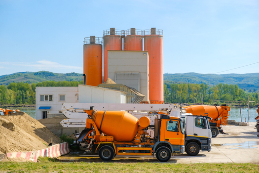 View of orange cement mixer trucks parked at a concrete plant with large silos under a clear blue sky in Novi Sad Vojvodina Serbia. View of orange cement mixer trucks parked at a concrete plant with large silos under a clear blue sky in Novi Sad Vojvodina Serbia.