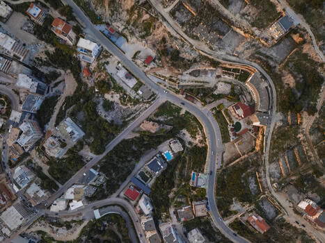 Aerial view of the town of Saranda featuring winding roads residential buildings with red tiled roofs and rocky terrain under warm golden hour light in Saranda Vlore County Albania. Aerial view of the town of Saranda featuring winding roads residential buildings with red tiled roofs and rocky terrain under warm golden hour light in Saranda Vlore County Albania.