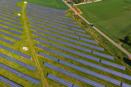Aerial view of a large solar farm with rows of photovoltaic panels installed on green grass fields with a road and surrounding agricultural landscape in Kyjov South Moravian Region Czechia.