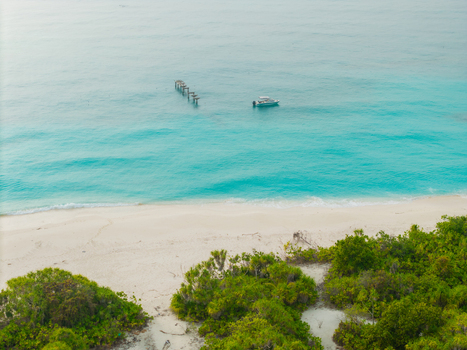 Aerial view of a serene beach meeting the turquoise sea where a boat rests near weathered wooden posts Hoarafushi Thiladhunmathee Uthuruburi Maldives. Aerial view of a serene beach meeting the turquoise sea where a boat rests near weathered wooden posts Hoarafushi Thiladhunmathee Uthuruburi Maldives.