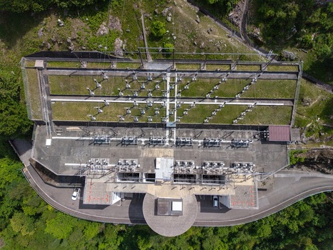 Aerial view of the Verzasca Dam power station infrastructure with electrical transformers and green terraces surrounded by lush forest in Gordola Ticino Switzerland. Aerial view of the Verzasca Dam power station infrastructure with electrical transformers and green terraces surrounded by lush forest in Gordola Ticino Switzerland.