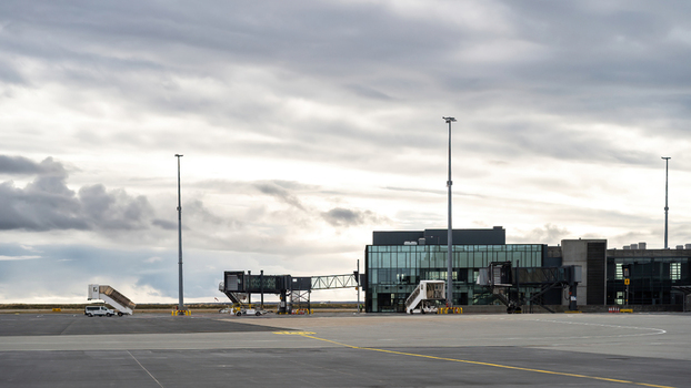 View of airport terminal building with jet bridges on the tarmac under a cloudy sky in Iceland.