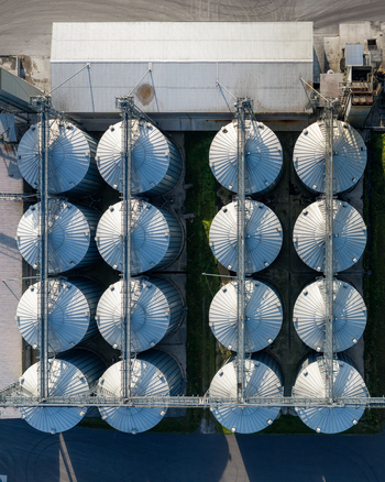 Aerial view of industrial grain silos arranged in a grid pattern with metallic surfaces and shadows in Slesin Greater Poland Voivodship Poland. Aerial view of industrial grain silos arranged in a grid pattern with metallic surfaces and shadows in Slesin Greater Poland Voivodship Poland.