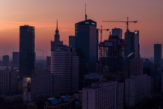 Warsaw Poland 01 March 2026 Aerial view of the city skyline at sunset with modern skyscrapers construction cranes and the Palace of Culture and Science under a glowing sky.