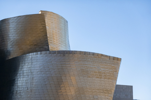 View of the shimmering titanium curves and metallic facade of the Guggenheim Museum Bilbao under a clear blue sky in Bilbao Euskadi Spain. View of the shimmering titanium curves and metallic facade of the Guggenheim Museum Bilbao under a clear blue sky in Bilbao Euskadi Spain.