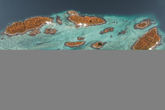 Aerial view of small islands with autumn foliage surrounded by turquoise coastal waters in Senja Troms Norway.