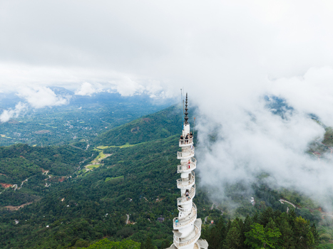 Aerial view of the white spiral Ambuluwawa Tower with people on its balconies rising above misty green mountains and clouds Gampola Central Province Sri Lanka. Aerial view of the white spiral Ambuluwawa Tower with people on its balconies rising above misty green mountains and clouds Gampola Central Province Sri Lanka.