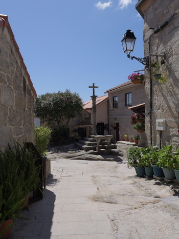View of the historic stone cross in the traditional village of Combarro with stone buildings and potted plants under a clear blue sky in Combarro Pontevedra Spain.