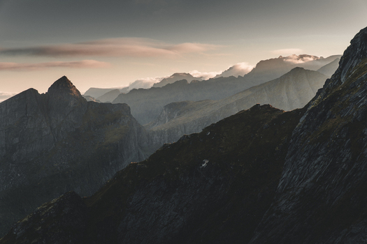 View of Reinebringen mountain peaks under soft golden light with dramatic clouds and rugged terrain in Moskenes Nordland Norway.