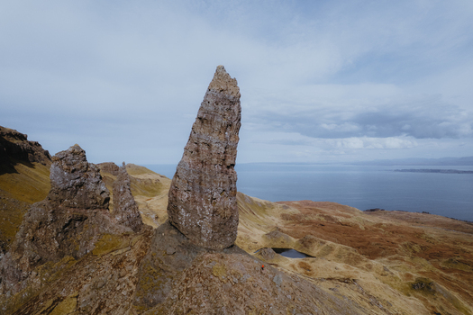 Aerial view of the iconic rock pinnacle known as The Storr rising above the rugged grassy slopes and cliffs overlooking the sea in Portree Scotland United Kingdom. Aerial view of the iconic rock pinnacle known as The Storr rising above the rugged grassy slopes and cliffs overlooking the sea in Portree Scotland United Kingdom.