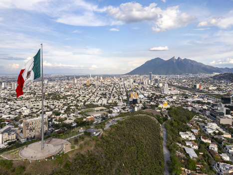 Aerial view of the large Mexican flag on a tall pole overlooking the urban cityscape of Monterrey with the Cerro de la Silla mountain in the background Monterrey Nuevo Leon Mexico.