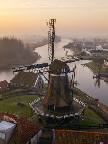 Aerial view of the historic De Kaai windmill standing by a calm canal during a misty sunrise in Sloten Friesland Netherlands. Aerial view of the historic De Kaai windmill standing by a calm canal during a misty sunrise in Sloten Friesland Netherlands.