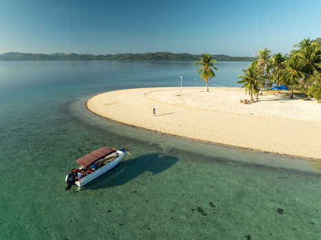 Aerial view of Pass Island featuring a white sand beach clear turquoise waters a small boat anchored near the shore and lush palm trees in Coron Philippines. Aerial view of Pass Island featuring a white sand beach clear turquoise waters a small boat anchored near the shore and lush palm trees in Coron Philippines.