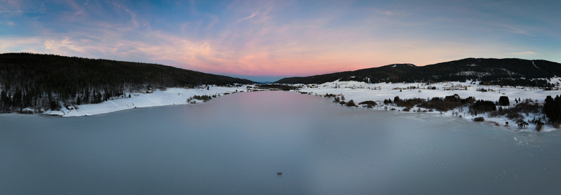 Aerial view of frozen lake reflecting the pastel sky bordered by snow covered forests and fields Les Rousses Bourgogne Franche Comté France. Aerial view of frozen lake reflecting the pastel sky bordered by snow covered forests and fields Les Rousses Bourgogne Franche Comté France.