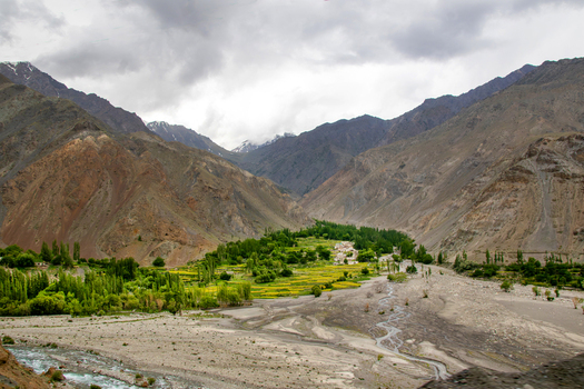 View of a lush green valley nestled between rugged mountains and a winding riverbed under a cloudy sky in Skardu Gilgit Pakistan. View of a lush green valley nestled between rugged mountains and a winding riverbed under a cloudy sky in Skardu Gilgit Pakistan.