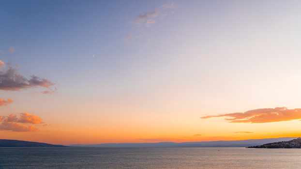 View of a serene sunset over Lake Geneva with soft orange and blue hues reflecting on the water and distant mountain silhouettes in Bourg en Lavaux Vaud Switzerland. View of a serene sunset over Lake Geneva with soft orange and blue hues reflecting on the water and distant mountain silhouettes in Bourg en Lavaux Vaud Switzerland.