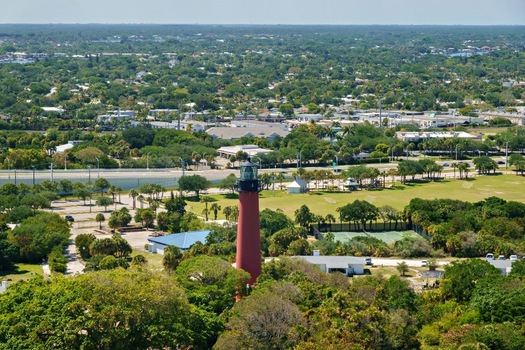 Aerial view of the red Jupiter Inlet Lighthouse surrounded by lush green trees and a park area with tennis courts in Jupiter Florida United States. Aerial view of the red Jupiter Inlet Lighthouse surrounded by lush green trees and a park area with tennis courts in Jupiter Florida United States.
