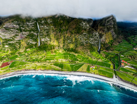Aerial view of dramatic cliffs meet the turquoise ocean waterfalls cascade down the vibrant green landscape a symphony of nature s artistry Faj&atilde; Grande Azores Portugal.