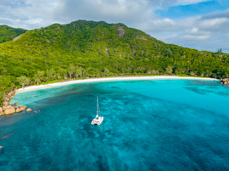 Aerial view of a catamaran anchored in turquoise waters off Anse Reunion beach with lush green hills and white sand coastline Anse Reunion La Digue Seychelles.