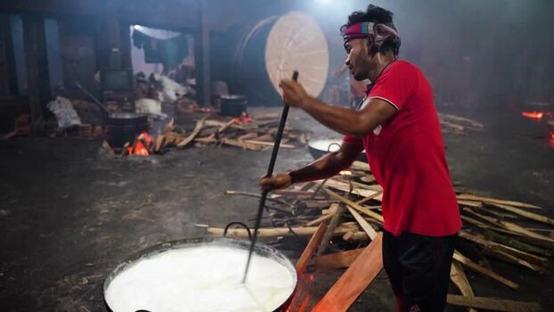 View of a man stirring milk in a traditional kitchen Bangladesh. View of a man stirring milk in a traditional kitchen Bangladesh.