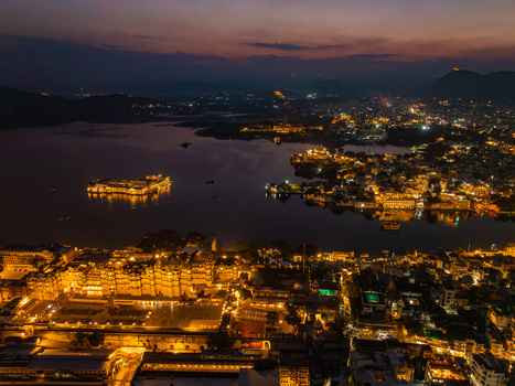 Aerial view of the illuminated City Palace and Lake Pichola at night with the Taj Lake Palace glowing in the water reflecting city lights in Udaipur Rajasthan India.