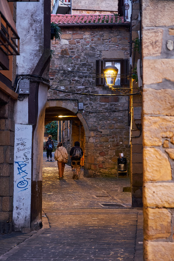 Pasai Donibane Spain 09 March 2026 View of people walking through a narrow historic stone street with an archway and a glowing street lamp in the old town.
