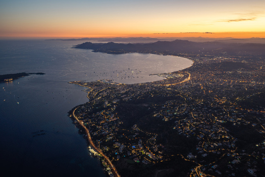 Aerial view of the illuminated coastline at twilight featuring the bay Mediterranean Sea and urban lights stretching along the shore in Antibes Provence Alpes Cote d Azur France. Aerial view of the illuminated coastline at twilight featuring the bay Mediterranean Sea and urban lights stretching along the shore in Antibes Provence Alpes Cote d Azur France.