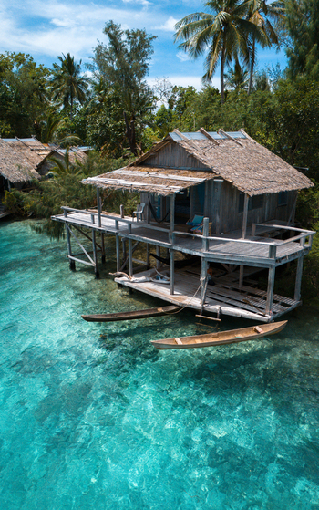 Aerial view of a rustic stilt house with a thatched roof sits above the crystal clear turquoise waters reflecting the lush greenery Gizo Western Province Solomon Islands. Aerial view of a rustic stilt house with a thatched roof sits above the crystal clear turquoise waters reflecting the lush greenery Gizo Western Province Solomon Islands.