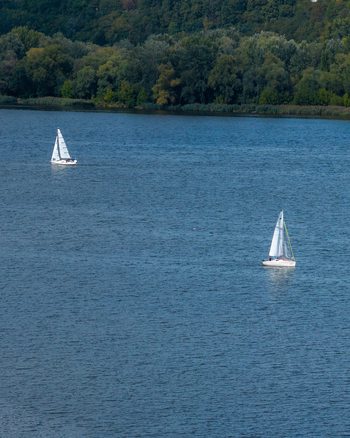 Aerial view of two sailboats racing on the Vistula river surrounded by lush green trees in Plock Masovian Voivodeship Poland.