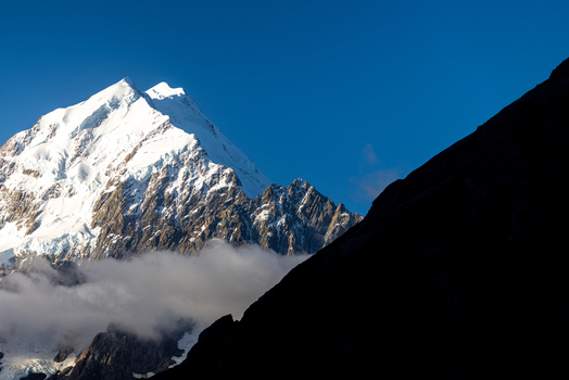 View of the majestic snow capped mountain piercing the clear blue sky a contrast to the dark shadowy foreground Mount Cook Canterbury Region New Zealand. View of the majestic snow capped mountain piercing the clear blue sky a contrast to the dark shadowy foreground Mount Cook Canterbury Region New Zealand.