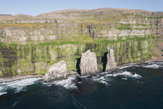 Aerial view of the Hornstrandir Nature Reserve featuring dramatic sea stacks and steep green cliffs with waves crashing against the shore Isafjordur Isafjardarbaer Iceland. Aerial view of the Hornstrandir Nature Reserve featuring dramatic sea stacks and steep green cliffs with waves crashing against the shore Isafjordur Isafjardarbaer Iceland.
