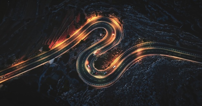 Aerial view of a winding S shaped road illuminated by streetlights at night with cars driving through rocky terrain in Malta Malta Malta. Aerial view of a winding S shaped road illuminated by streetlights at night with cars driving through rocky terrain in Malta Malta Malta.