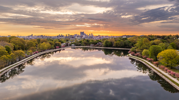Aerial view of Brookline Reservoir reflecting a colorful sunrise sky with the Boston skyline on the horizon and spring trees along the shore Brookline Massachusetts United States.
