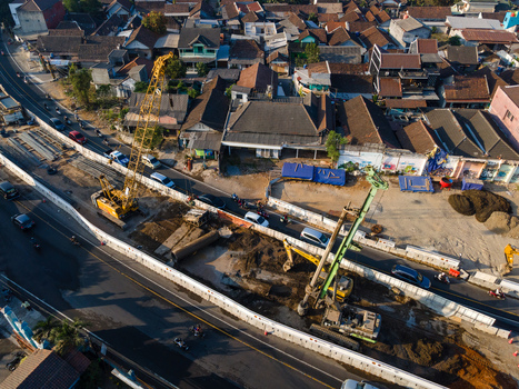 Aerial view of a road construction site with cranes and excavators working on a busy urban street surrounded by residential houses in Yogyakarta Special Region of Yogyakarta Indonesia. Aerial view of a road construction site with cranes and excavators working on a busy urban street surrounded by residential houses in Yogyakarta Special Region of Yogyakarta Indonesia.