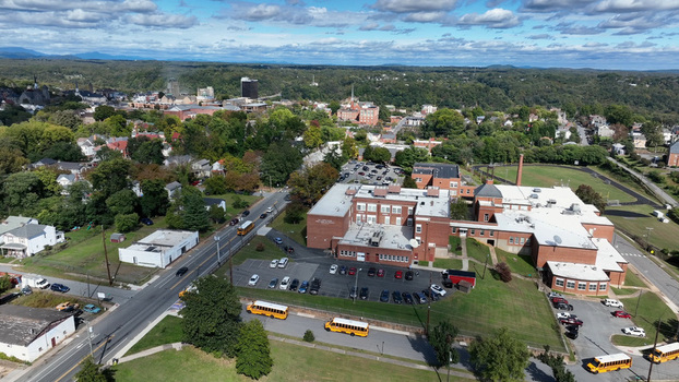 Aerial view of a school building with yellow school buses parked in the lot surrounded by residential houses trees and roads in Lynchburg Virginia United States.