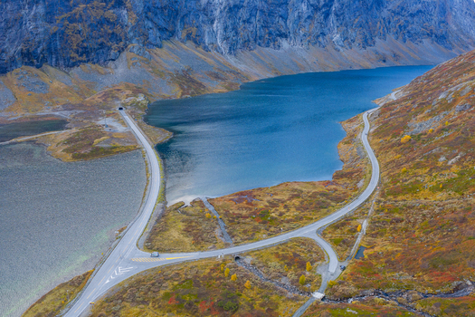 Aerial view of Skjakvegen winding through a dramatic mountain landscape with a deep blue lake and vibrant autumn foliage in Skjak Innlandet Norway. Aerial view of Skjakvegen winding through a dramatic mountain landscape with a deep blue lake and vibrant autumn foliage in Skjak Innlandet Norway.